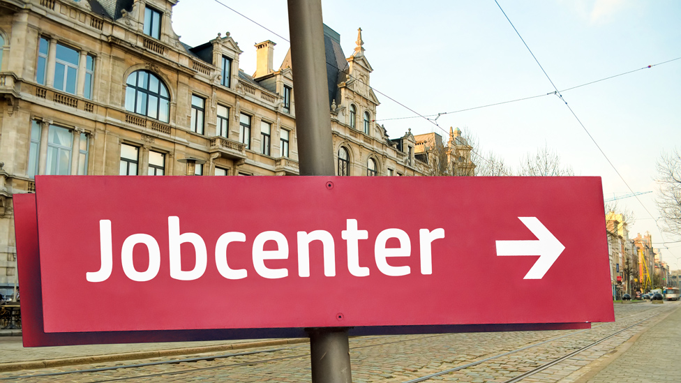 Finanzielle Hilfen vom Jobcenter (Quelle: Thomas Reimer - stock.adobe.com) Hinweiß Schild Jobcenter vor Hintergrund einer Altstadt