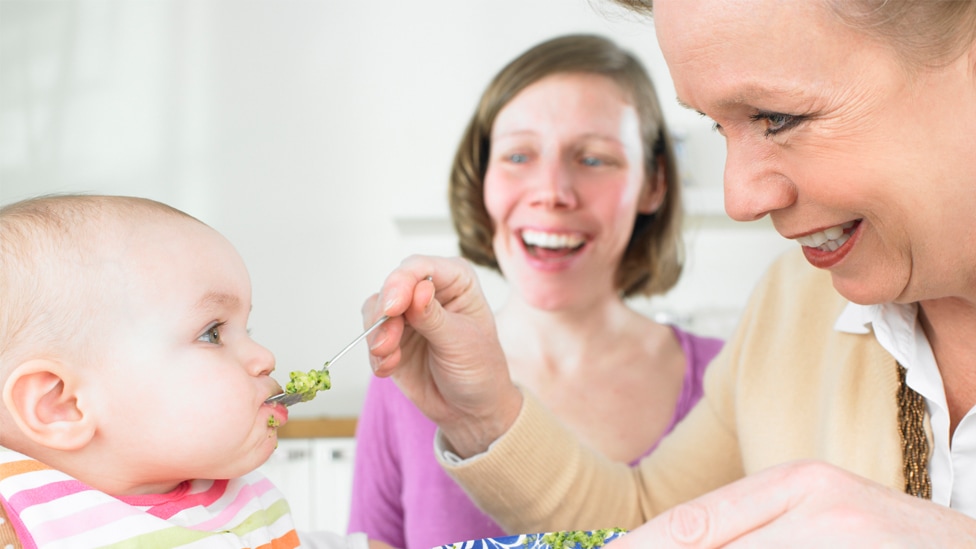 Großmutter füttert ihr Enkelkind mit Brei, Mutter schaut zu
