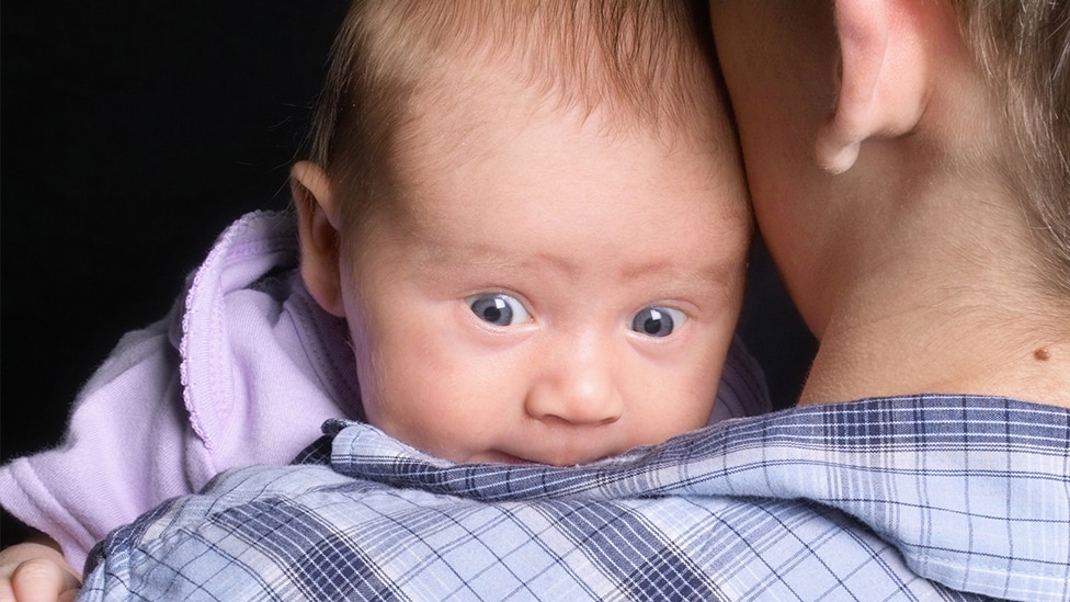 Die ersten Tage (Quelle: iStock.com/jhorrocks) Baby liegt mit dem Kopf auf der Schulter seines Vaters