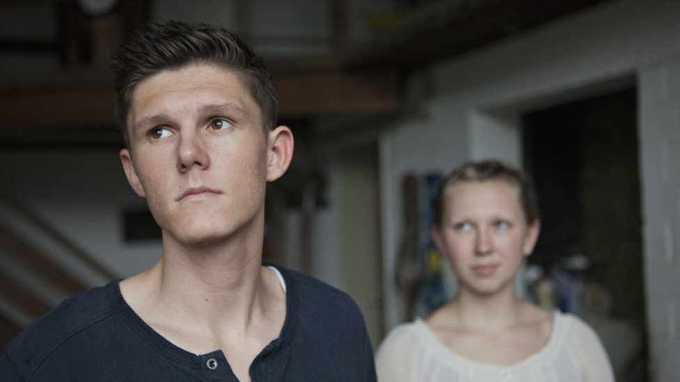 Junger Mann schaut nachdenklich, seine Freundin steht hinter ihm