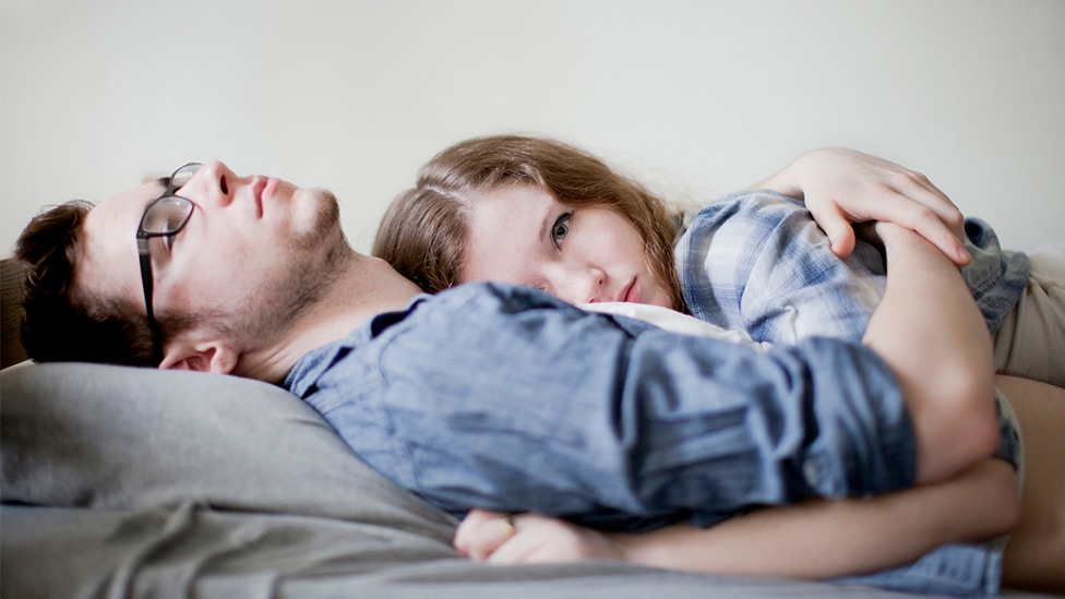 Sie ist schwanger - was nun? (Quelle: Shestock / via Getty Images) Junges Paar liegt Arm in Arm nachdenklich auf einem Sofa